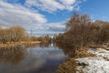 Fototapeta na wymiar Spring flood. High water. Church on the banks of the river. Rural landscape in early spring. Clouds and trees reflected in the water.