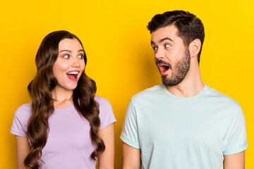 Portrait of lovely amazed cheerful couple looking at each other good mood isolated over bright yellow color background