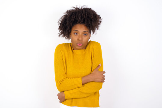 young beautiful African American woman wearing yellow sweater against white wall shaking and freezing for winter cold with sad and shock expression on face.