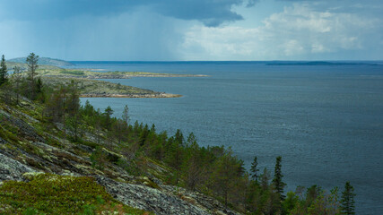 View of the sea and sky from a high point. Harsh northern nature. Rocky island overgrown with forest, dramatic sky with rain clouds. Beautiful view of the White Sea, Russia.