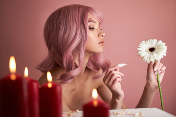 Obraz na płótnie Canvas Beautiful woman with dyed pink hair guessing at flower in hand at table with candles. Pink beauty hair on head of woman fortune teller. Beauty Girl with flower in her hand