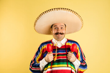 Happy man in sombrero and bright poncho isolated over yellow background