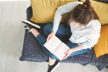 young beautiful woman sitting on a sofa at home and reading a book