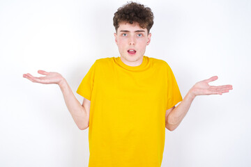 Fototapeta premium young caucasian handsome man with curly hair wearing yellow T-shirt against white studio wall celebrating crazy and amazed for success with arms raised and open eyes screaming excited. Winner concept