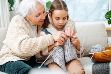 Skillful granny tutoring her granddaughter, teaching her how to knit