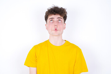 young caucasian handsome man with curly hair wearing yellow T-shirt against white studio background  making fish face with lips, crazy and comical gesture. Funny expression.