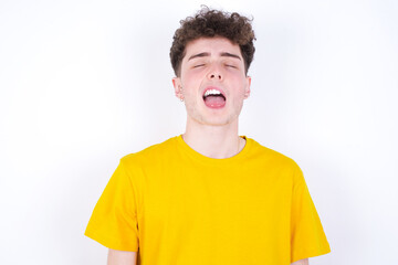 young caucasian handsome man with curly hair wearing yellow T-shirt against white studio background  sticking tongue out happy with funny expression. Emotion concept.