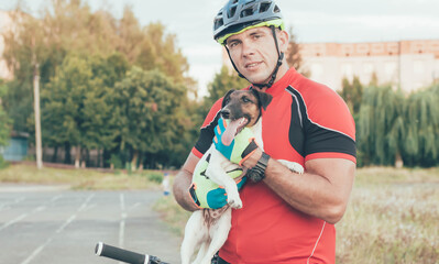 sporty man sits on a bicycle and holds a dog in his hands in the city at the stadium