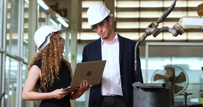 Manufacturing Factory female Mechanical Engineering programer Works on Personal Computer and man worker are working with Robotic Arm at industrial factory