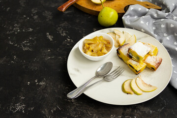 Sliced pie on a white plate with pear jam on a black table. Green pears in the background are blurred. Morning breakfast