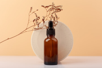 Selective focus, skin serum against round podium with dry plant on white table against beige...