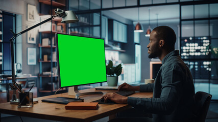 Handsome Black African American Specialist Working on Desktop Computer with Green Screen Mock Up Template Display at Home Living Room. Freelance Man Connects to Clients Over the Internet.