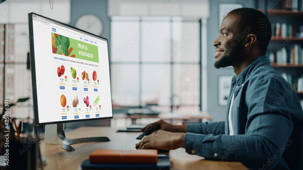 Sticker handsome black african american is using desktop computer with groceries delivery web page to order 