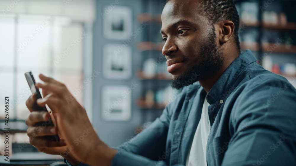 Poster excited black african american man using smartphone while sitting at table in living room. happy man
