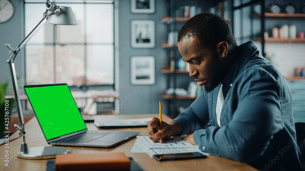 Poster african american man having an online video lesson on laptop computer with mock up green screen in l