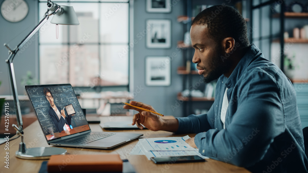 Poster african american man having an online video lesson on laptop computer while sitting behind desk in l
