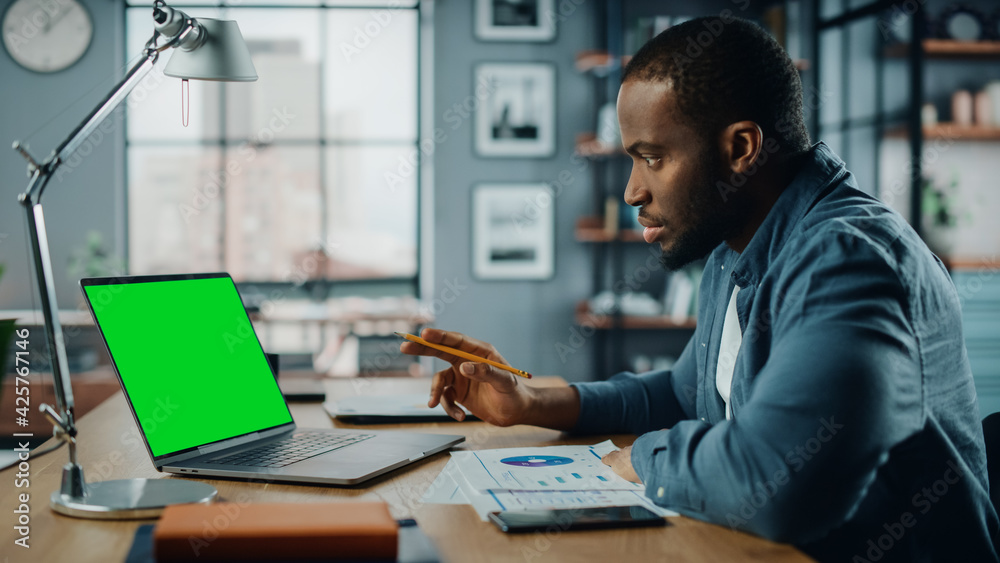 Poster african american man having an online video lesson on laptop computer with mock up green screen in l