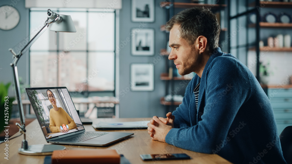 Aufkleber Handsome Caucasian Man Having a Video Call on Laptop Computer while Sitting Behind Desk in Living Room. Freelancer Working From Home and Talking to Colleagues and Clients Over the Internet.