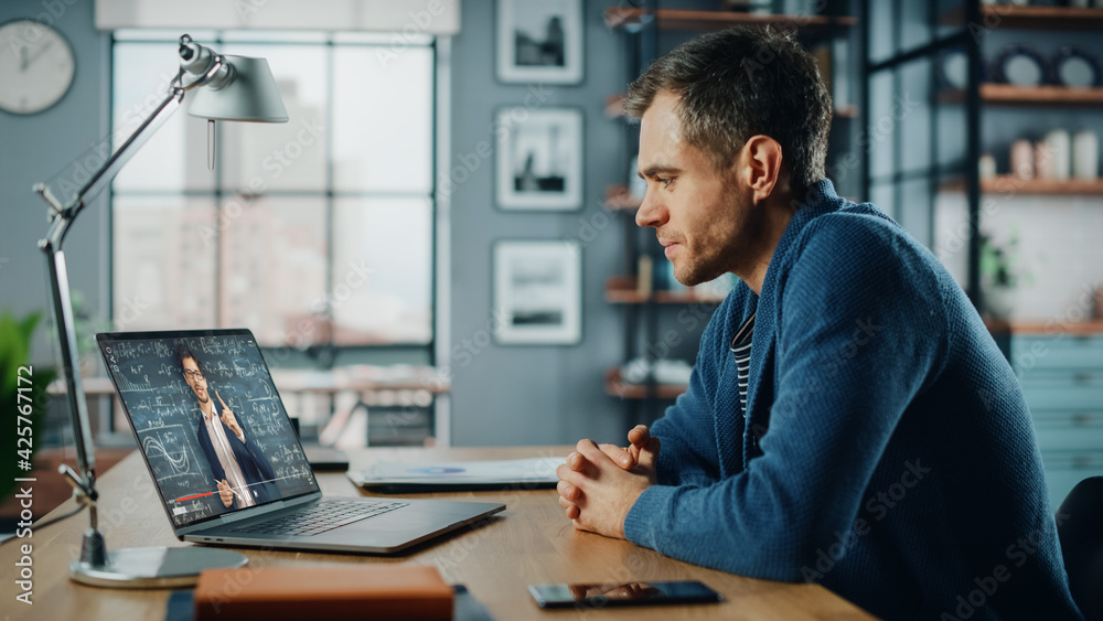 Poster handsome caucasian man having an online video lesson on laptop computer while sitting behind desk in