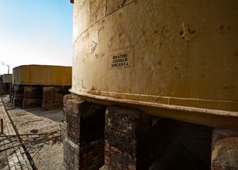 Demolition of outdated Soviet sulfuric acid plant.Old rusted yellow steel storage tanks for acid. Title on tank: Danger. Sulfuric Acid.