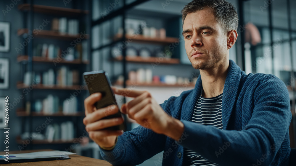 Leinwandbilder serious caucasian man using smartphone while sitting at a desk in stylish living room. young man smi