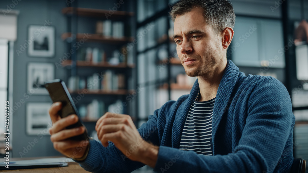 Leinwandbilder serious caucasian man using smartphone while sitting at a desk in stylish living room. young man smi