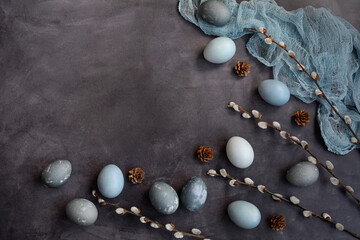 Flat lay, copy space. Easter composition on a gray background. Blue, marble and gray eggs, willow branches and a napkin. View from above