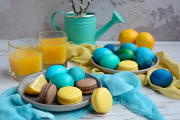 Painted yellow, blue, green eggs on plates and multi-colored macarons on a light rustic background. Easter composition