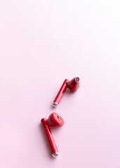 Red wireless headphones on pink background with copy space
