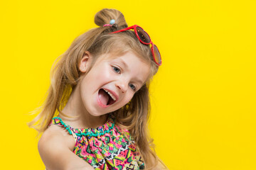 Cute little girl in sun glasses on the yellow background in the studio.