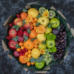 A large bouquet of fruits. Grapes, apples, oranges, kiwi, tangerines, pomegranates and flowers. View from above .