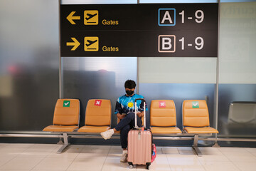 Asian traveller wearing protective mask using smartphone searching airline flight status and...