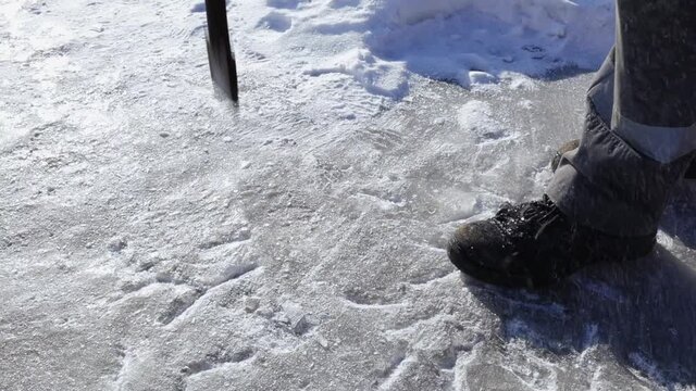 The worker hits the ice with a crowbar and splashes and snow crystals fly. Close-up from the bottom point of the image. Cleaning the sidewalk surface from ice.