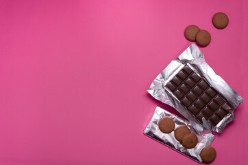 Top view of whole chocolate bars, sweet round cookies on the pink surface.Empty space