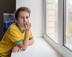 A little boy looks out the window from the house.