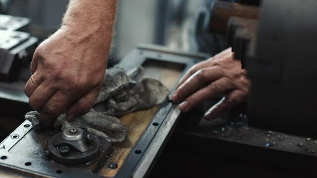 Service and repair of machine tools in a machine shop or workshop. These are the hands of a white man with a rag wiping the metal parts of a lathe engine with grease. The work of a locksmith on