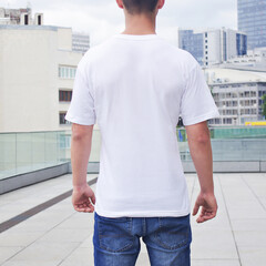 white t-shirt mockup back view, young man wearing a white t-shirt on a blurred city background