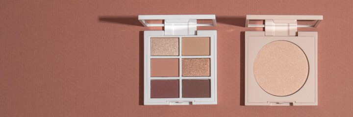 Eye shadow palette and highlighting powder on pink clean background with hard light. Sunlight