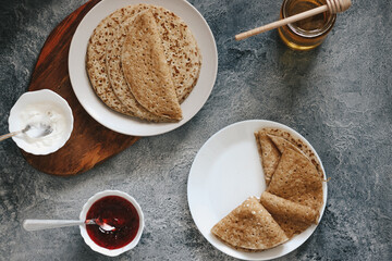 pancakes with honey and jam and fresh berries stand on a gray background, copyspace