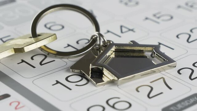 Key with a house shaped keychain and wall calendar with circled day of month. Buying or selling a house, real-estate agency, home insurance, rent, concepts