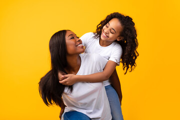 African American girl hugging her smiling mom from behind