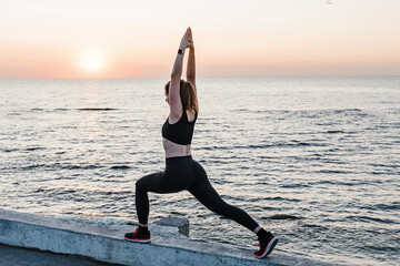 Fototapeta na wymiar Young woman doing yoga or making exercises near the sea at sunrise.