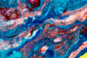 The background is acrylic blue with red and pink stains sprinkled with sparkles. Colorful marble texture. Fluid liquid marble. Art picture. Avant-garde contemporary art.