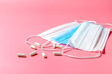 Disposable surgical masks and pills on the table. Pink background. View from above. Place for your text. High quality photo