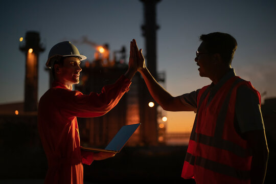 Happy employee raise their hands and shout for joy in power plant at night.