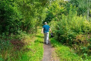 forest path with tall grass. a man walks down the road and carries dirty rubber boots