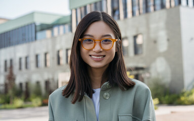 Authentic portrait of young beautiful woman wearing stylish eyeglasses.   Smart asian student standing in university campus looking at camera, smiling. Education concept 