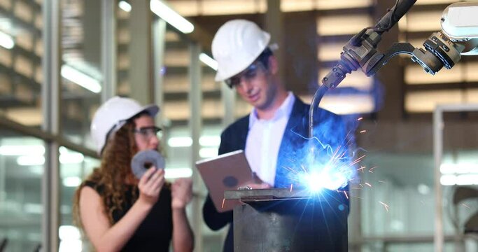 Manufacturing Factory female Mechanical Engineering programer Works on Personal Computer and man worker are working with Robotic Arm at industrial factory