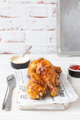 Roasted chicken legs drumsticks on wooden board with newspaper sheet served with ketchup and...