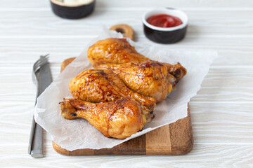 Roasted golden chicken legs drumsticks on baking paper on wooden board served with ketchup and...